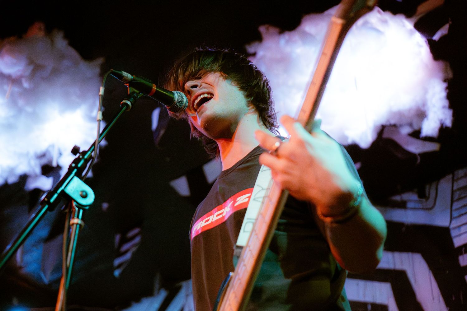 Concert performer singing passionately into microphone on dimly lit stage with dramatic red and blue lighting effects.