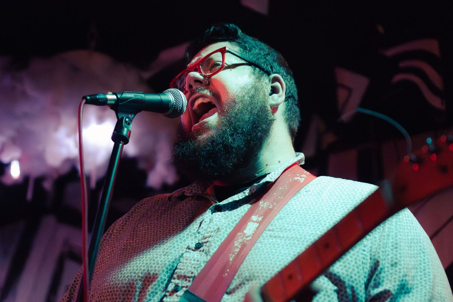 Singer performs passionately on stage with microphone in dark concert lighting with red and blue hues.