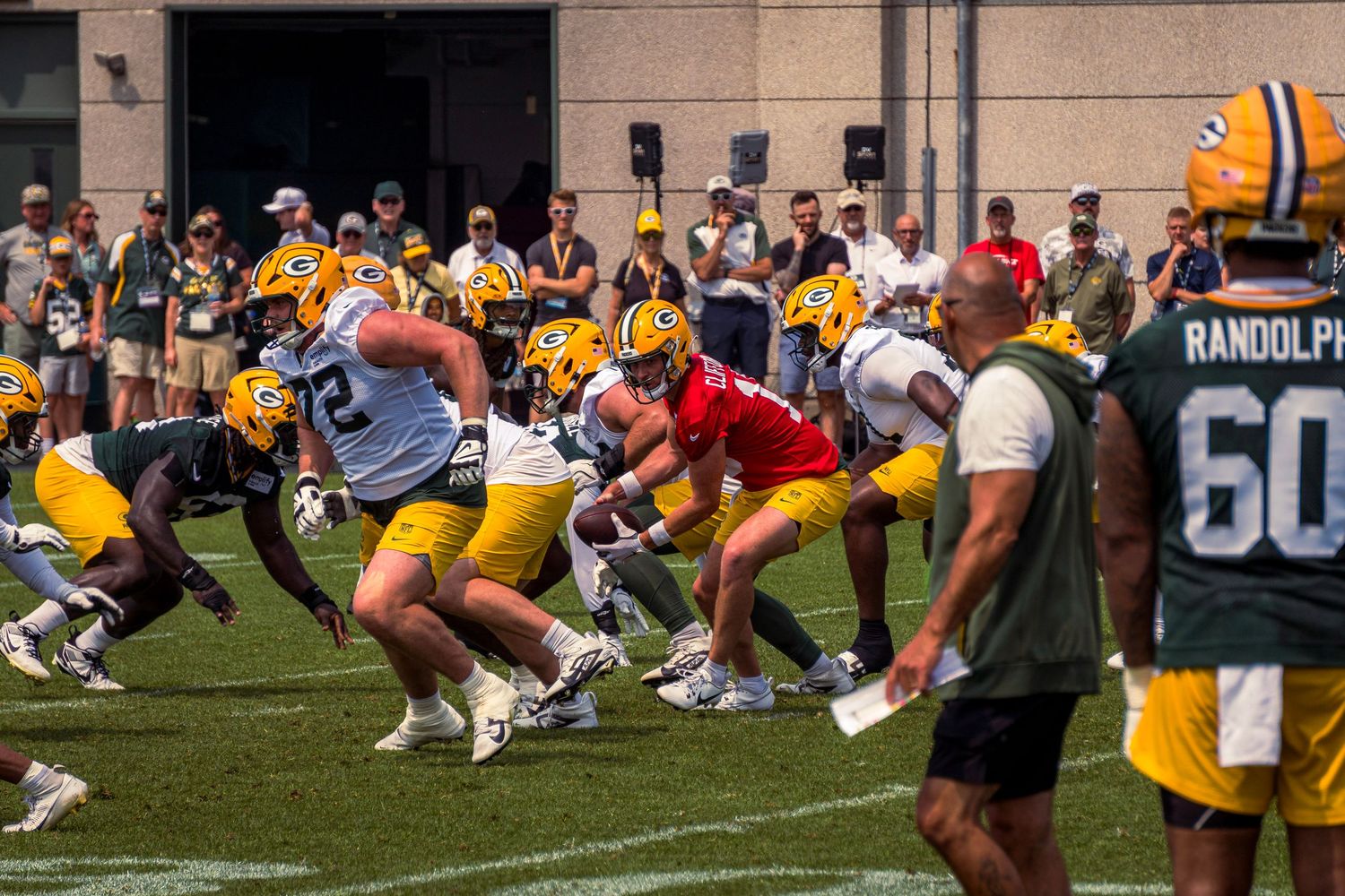 Football players line up in practice formation on a sunny field during training camp.