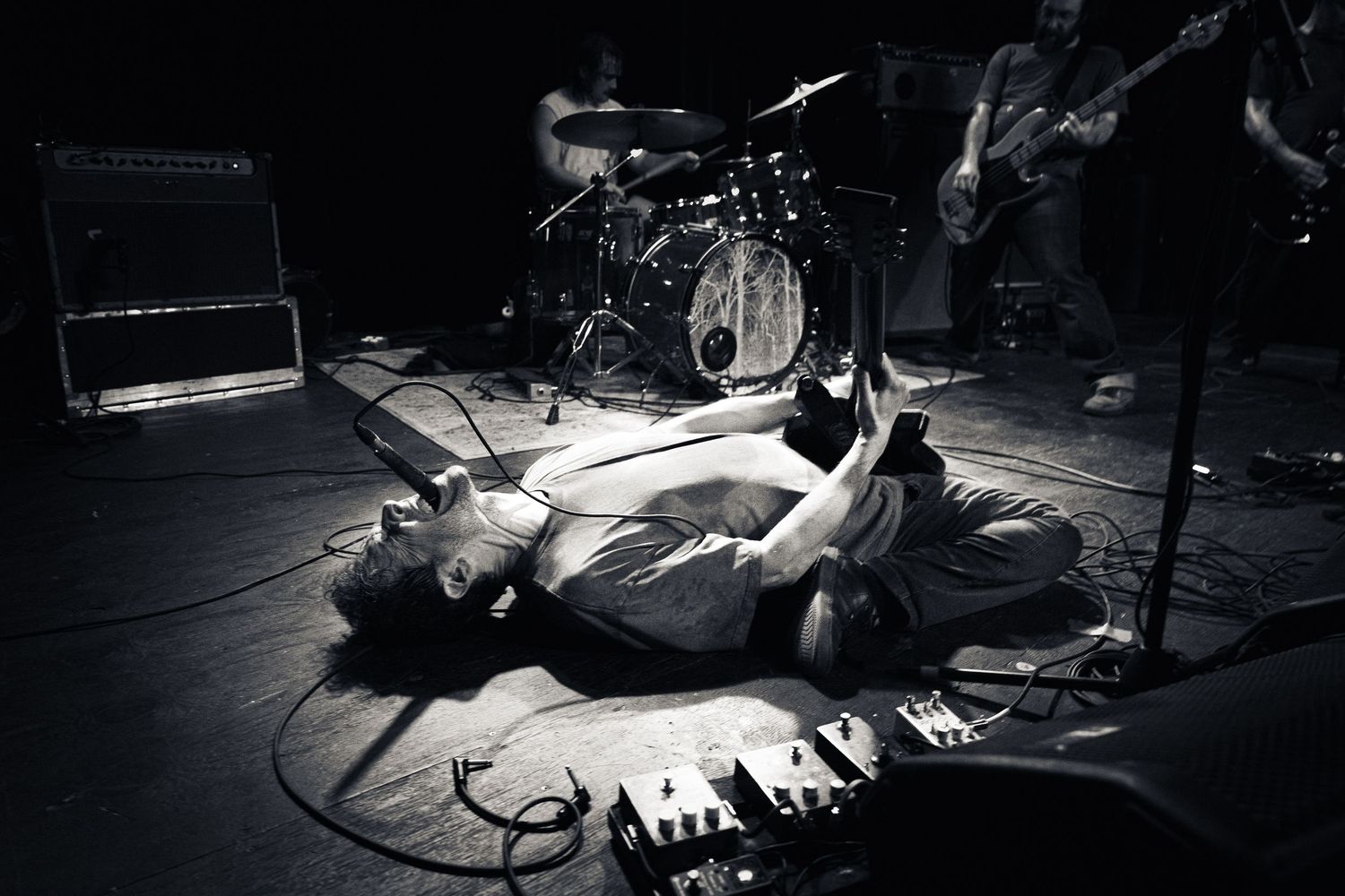 Black and white photo of a guitarist lying on stage during a live rock concert performance.