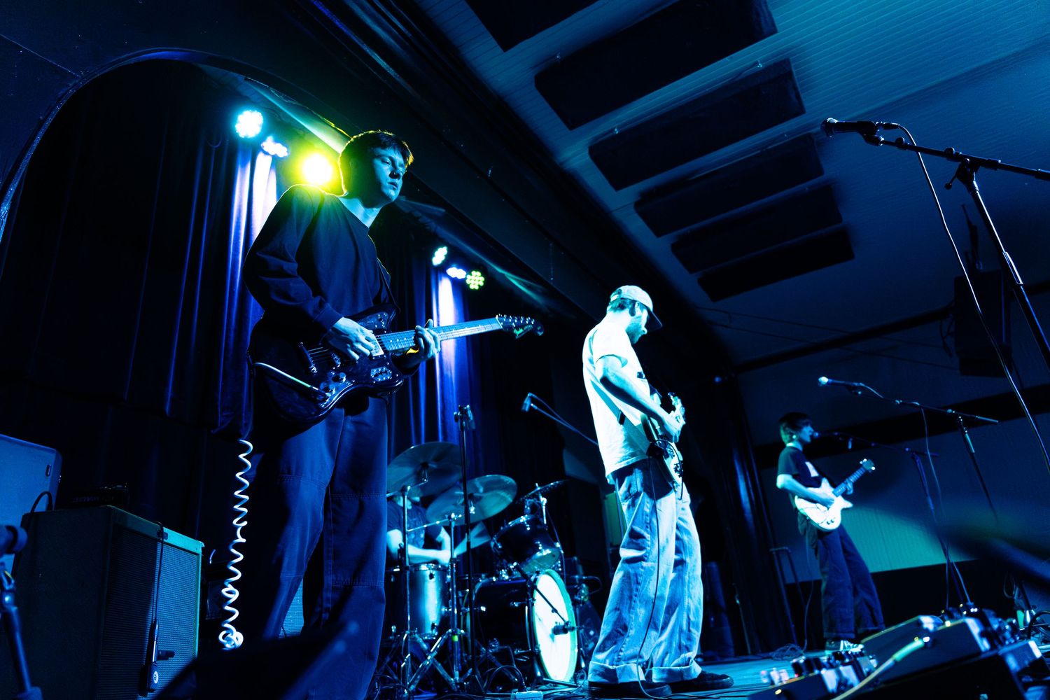 Musicians perform on stage under dramatic blue and green lighting during a live concert performance.