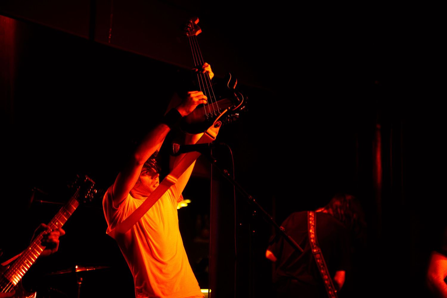 A dramatic silhouette of a guitarist performing on stage illuminated by red and orange lighting effects.