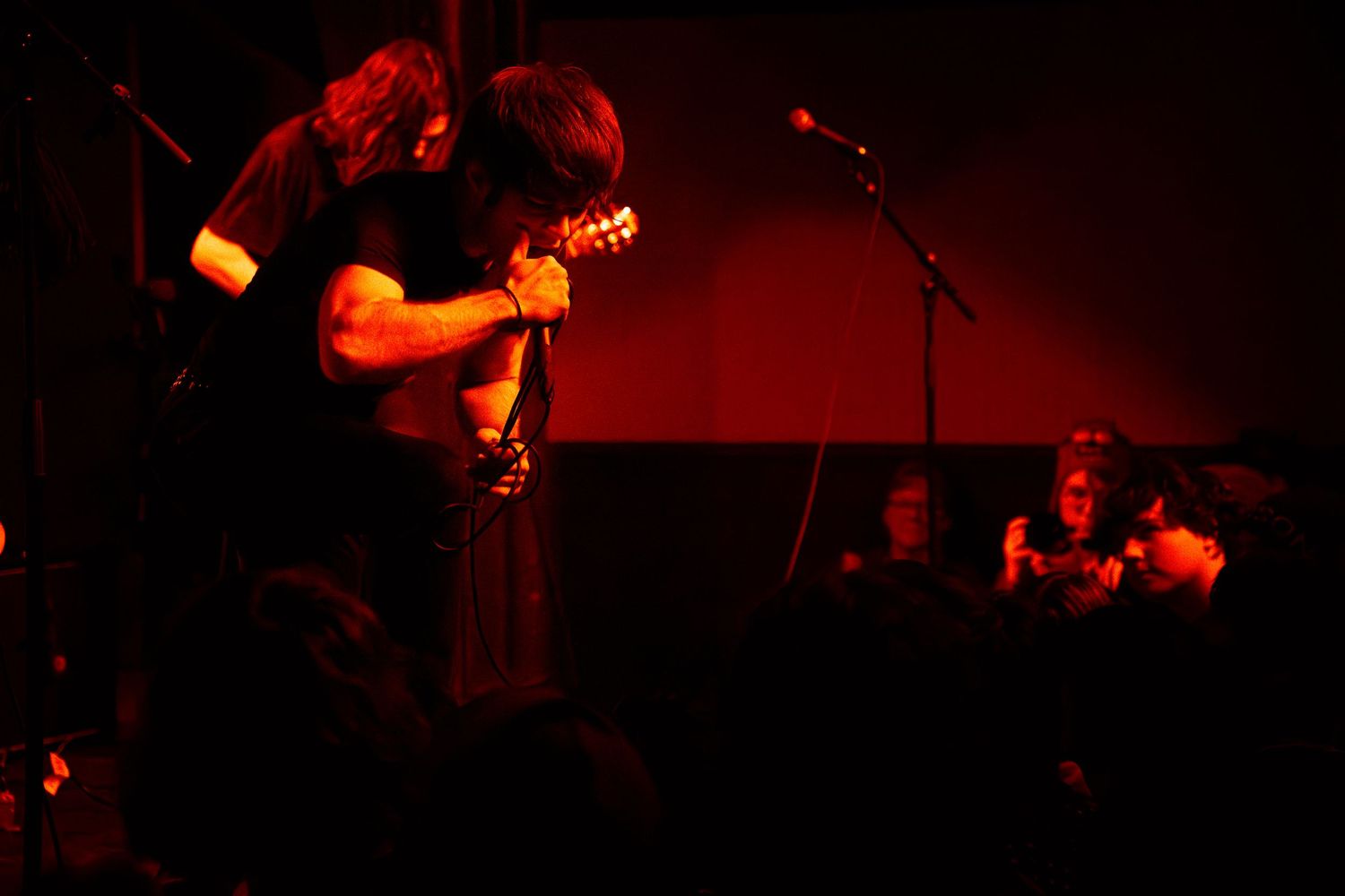 A rock band performs on stage with dramatic red lighting and silhouetted figures creating an energetic atmosphere.