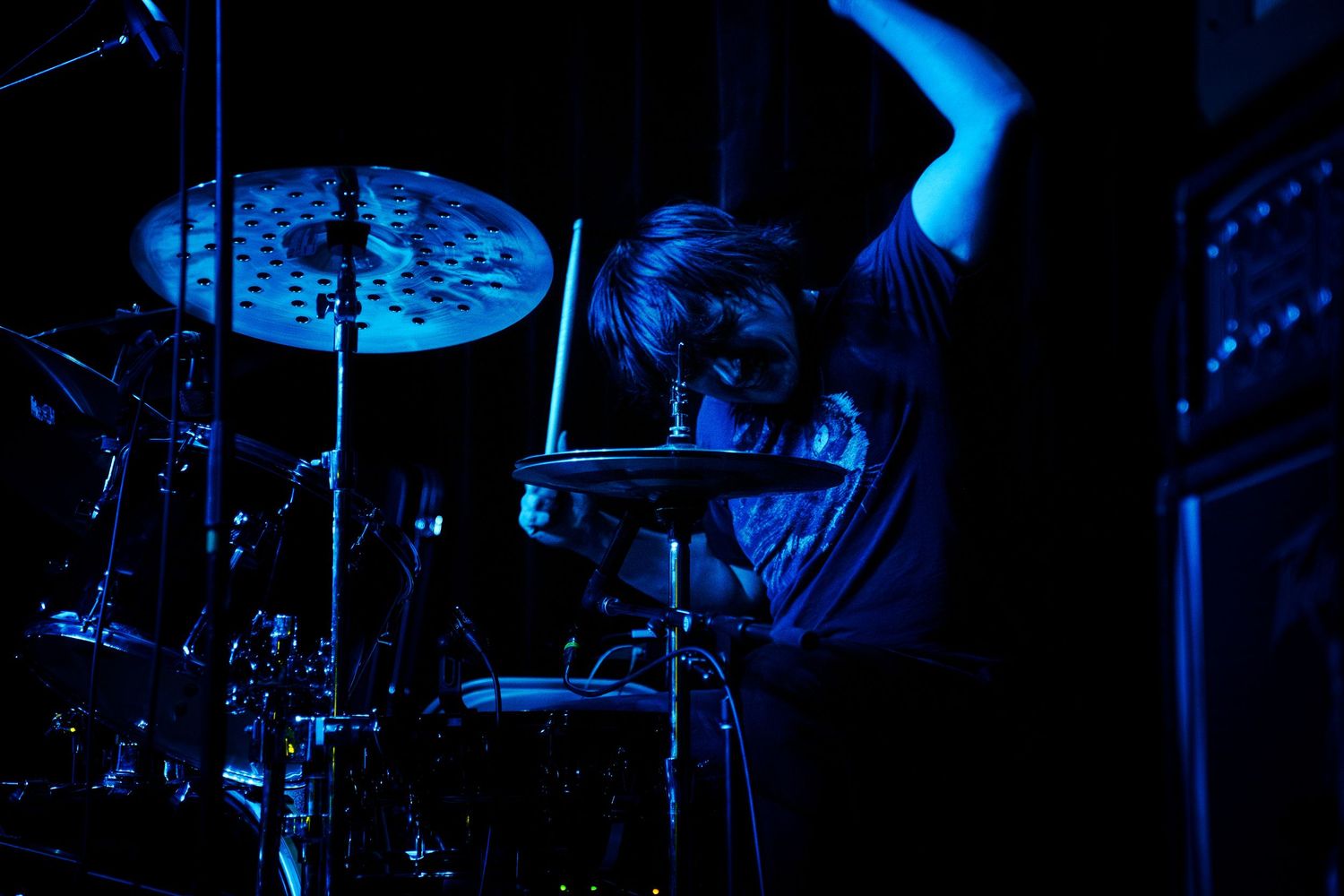 Illuminated blue stage lights shine through darkness during a concert performance.