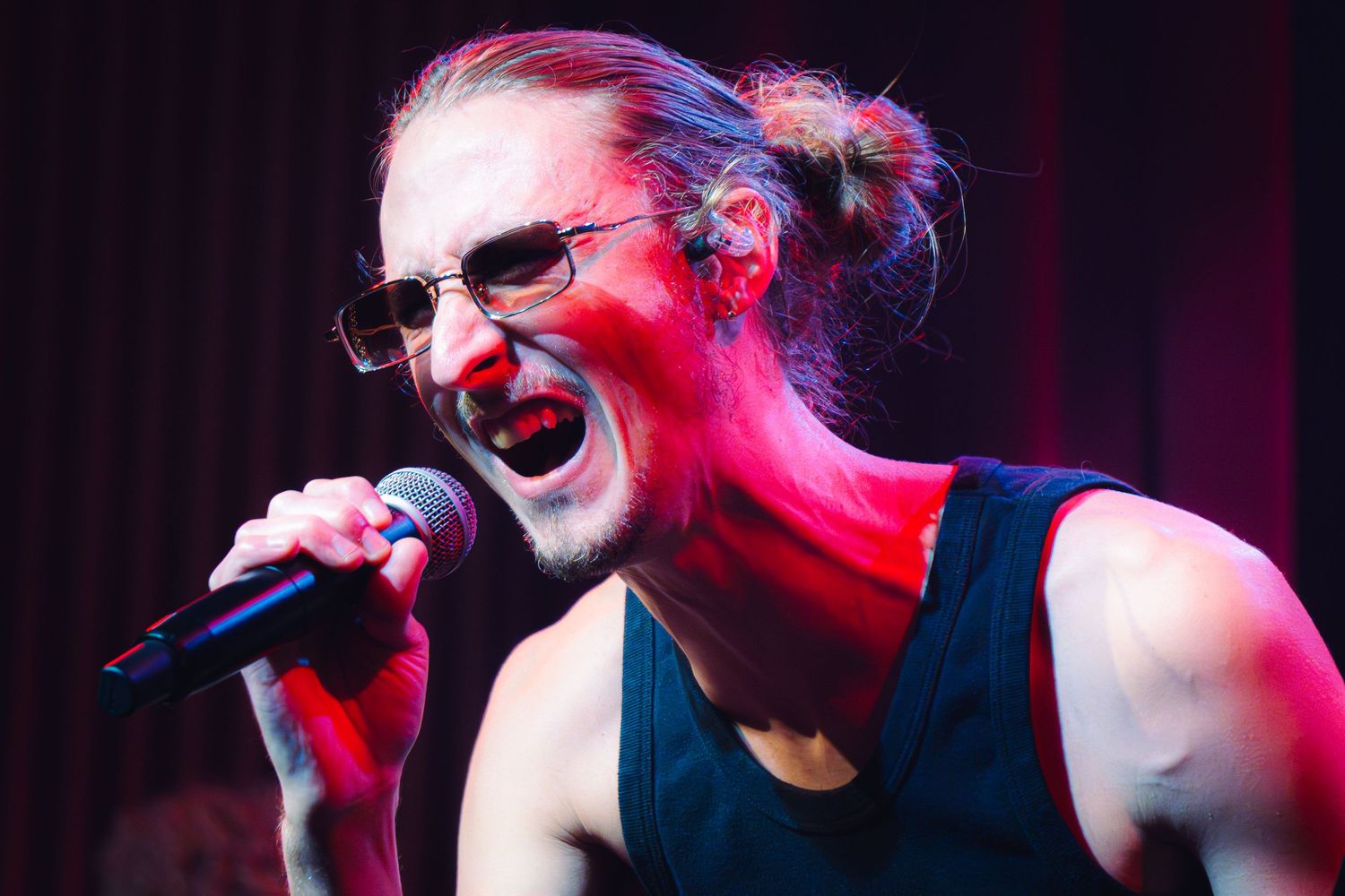 A performer sings passionately on stage with dramatic red lighting creating an energetic concert atmosphere.