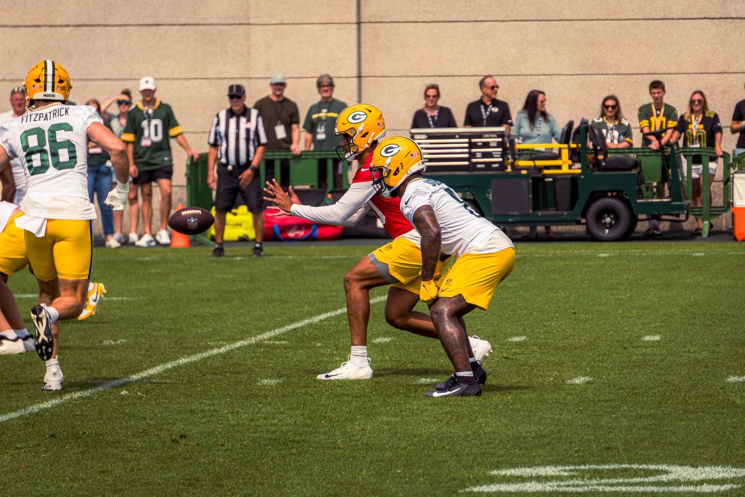 Football players in yellow and white uniforms engage in a play during a game on a grass field with spectators watching.