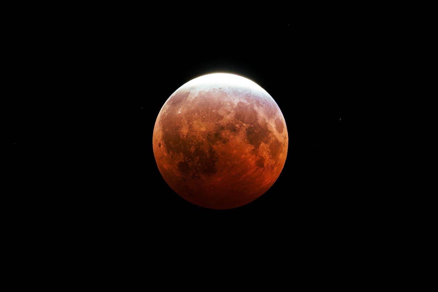 A stunning blood moon lunar eclipse glowing in vivid red and orange hues against a dark black night sky.