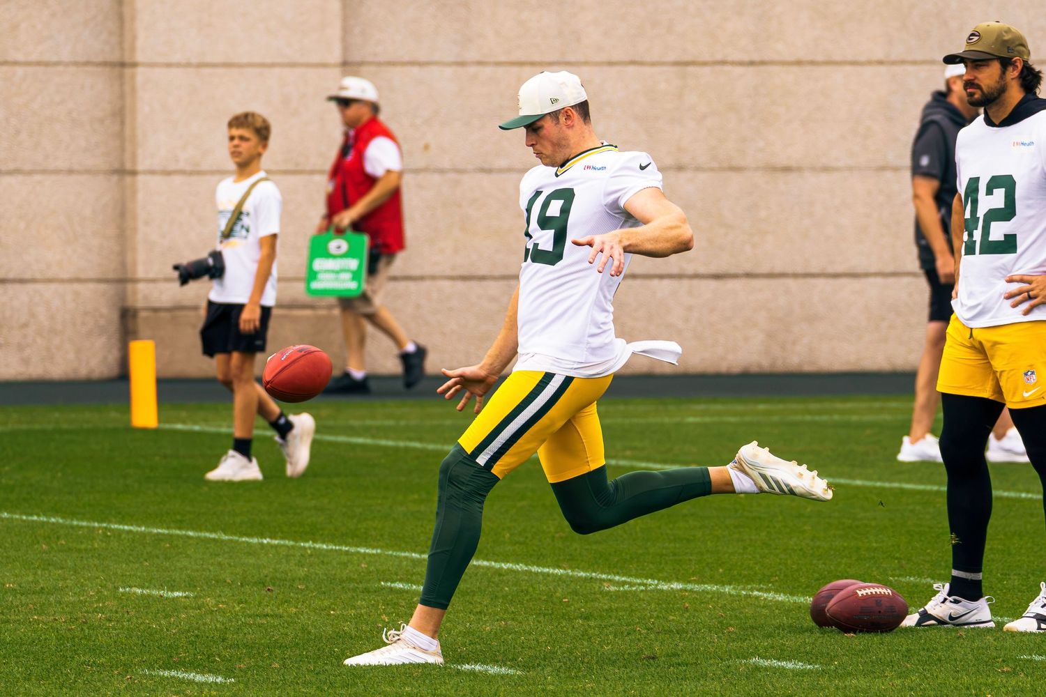 Green Bay Packers player #19 kicking a football during NFL training camp practice on an outdoor field.