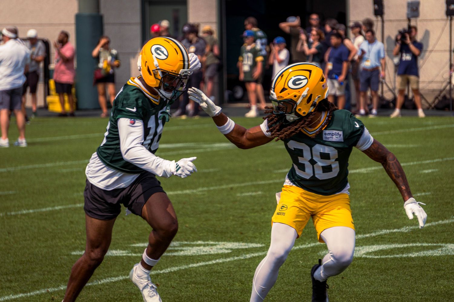 Green Bay Packers players practice football drills during training camp on a sunny day.