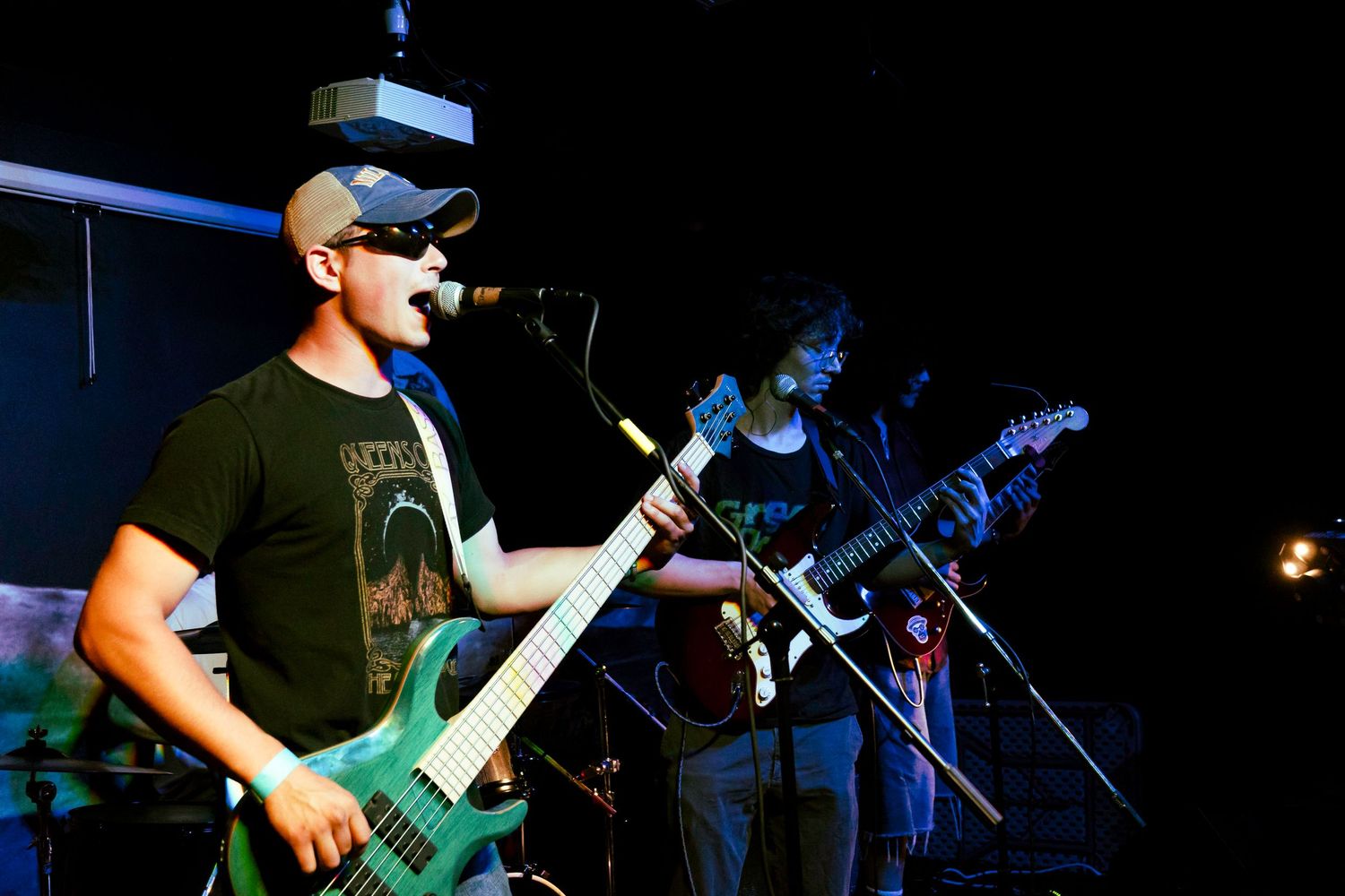 Rock band performs on a dark stage with dramatic blue lighting and guitar players in silhouette.