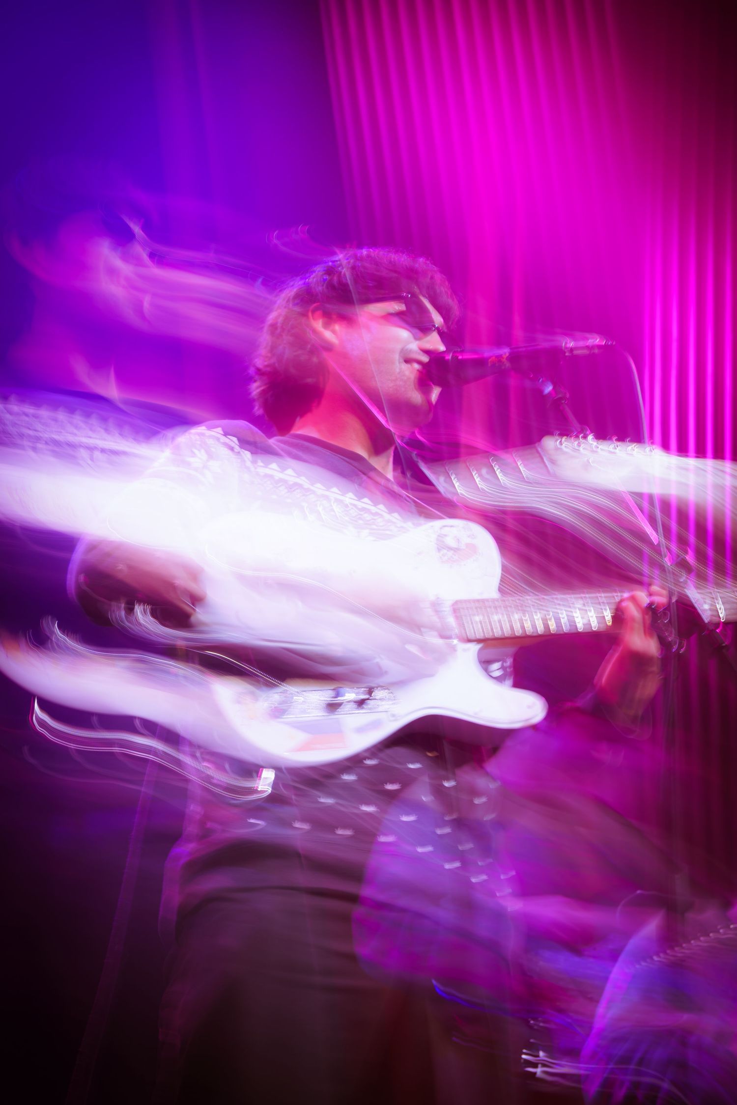 Motion-blurred electric guitar in vibrant purple stage lighting creates an energetic performance atmosphere.