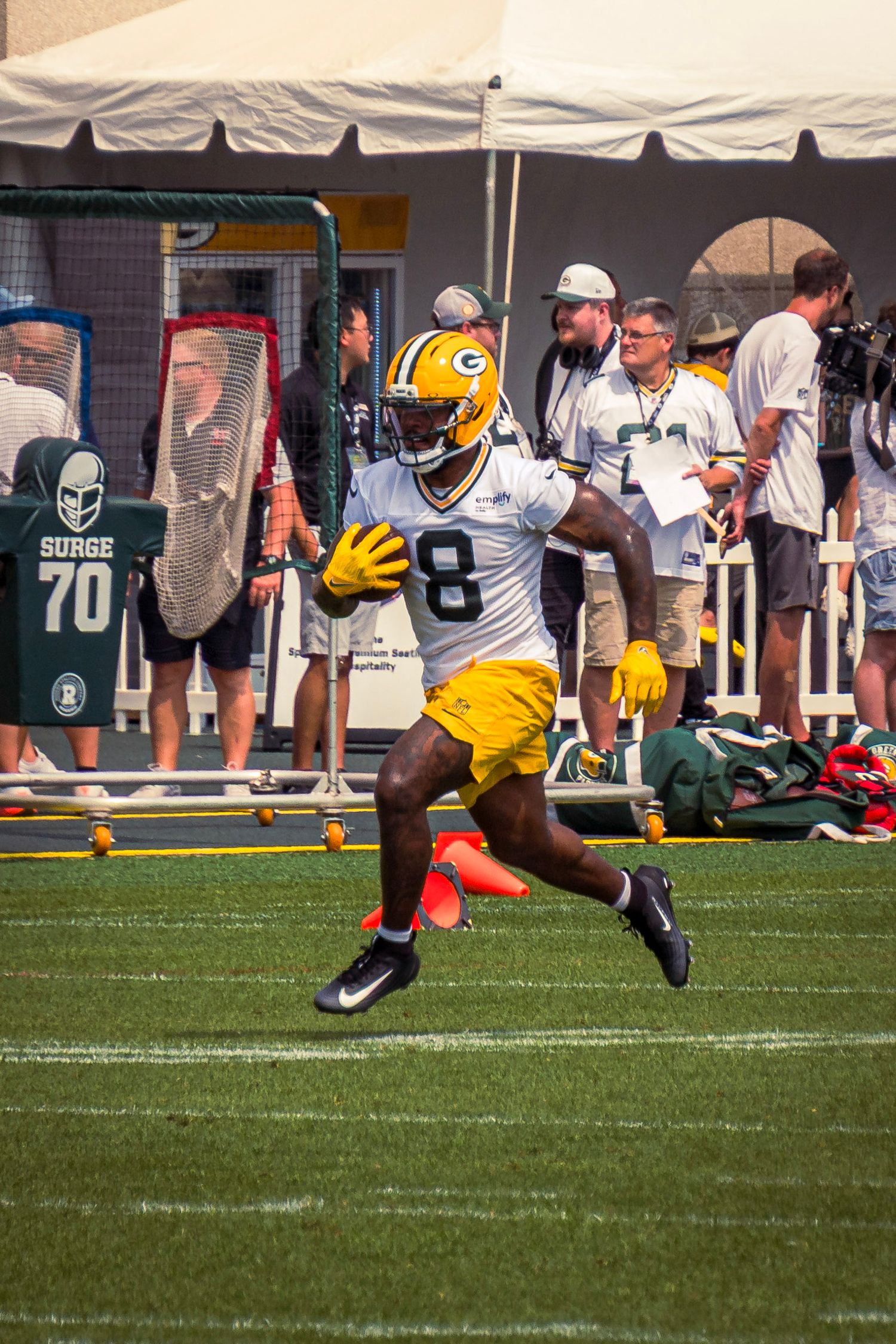 Green Bay Packers player in yellow jersey number 8 runs across football field during training camp practice.