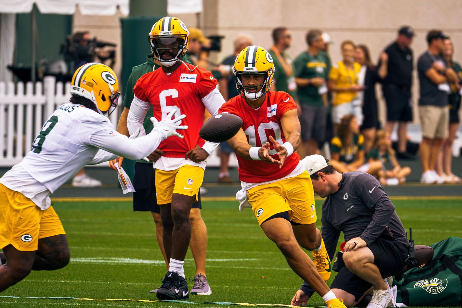Green Bay Packers players practice handoffs in yellow jerseys during NFL training camp on an outdoor field.