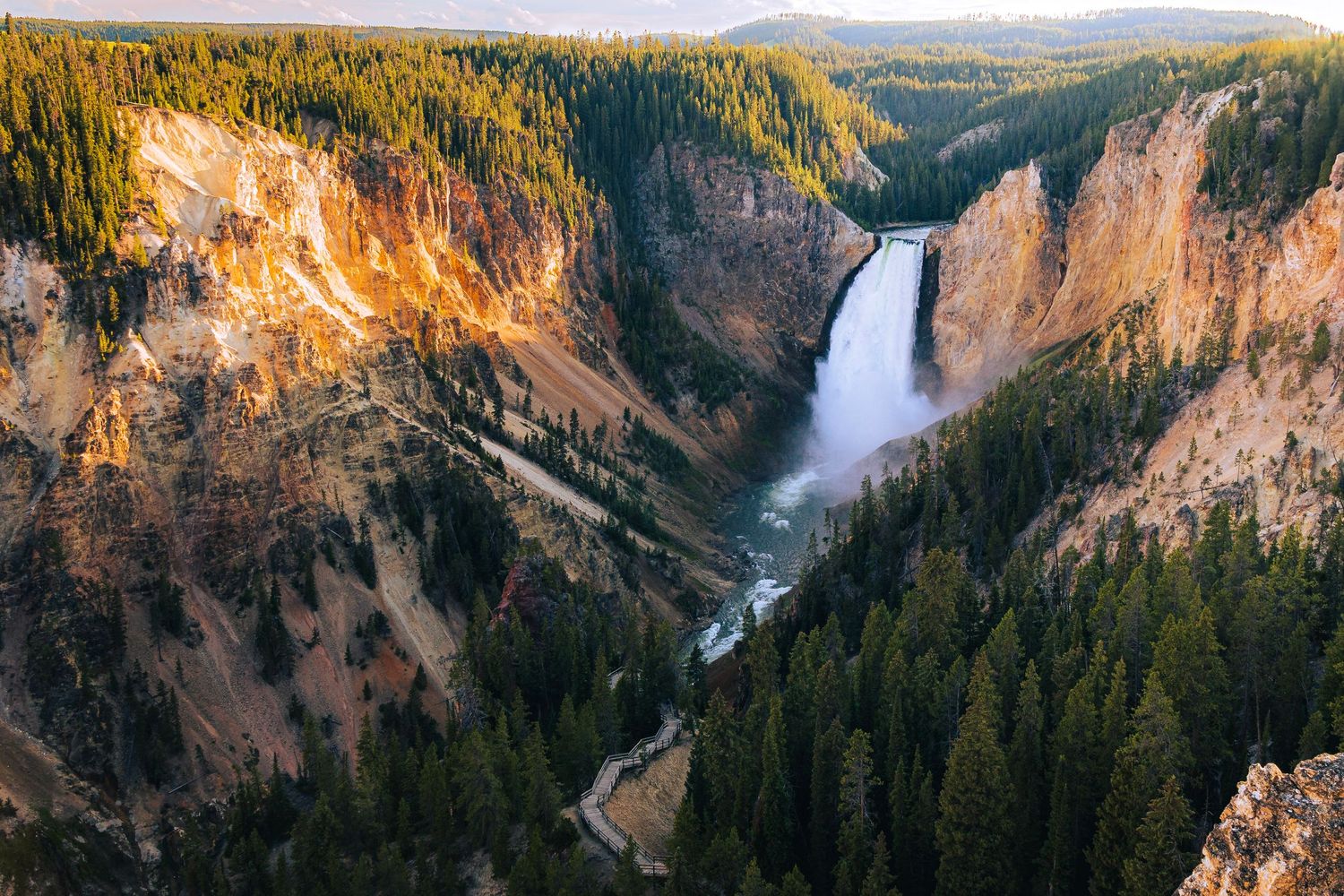 Scenic view of Lower Falls waterfall cascading through the Grand Canyon of Yellowstone surrounded by golden cliffs.