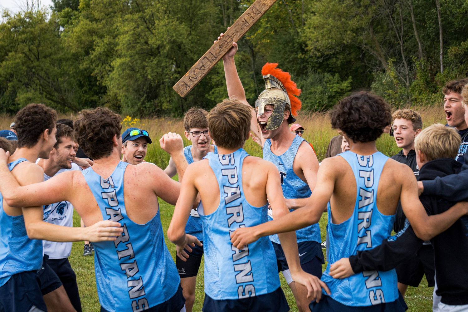 Cross country team in light blue jerseys celebrates together after a race.