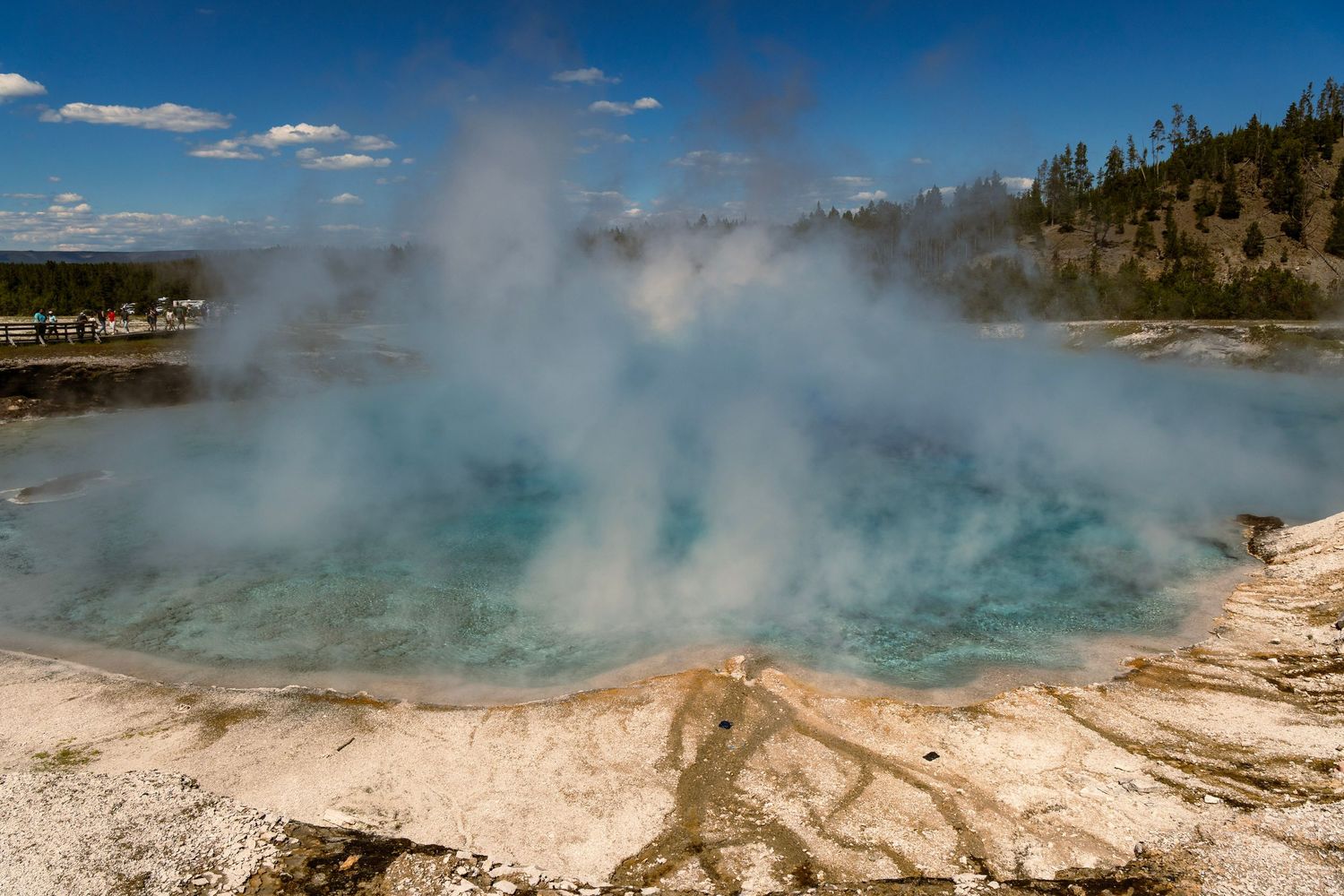 Steam rises from vibrant turquoise geothermal hot springs surrounded by mineral deposits in Yellowstone National Park.