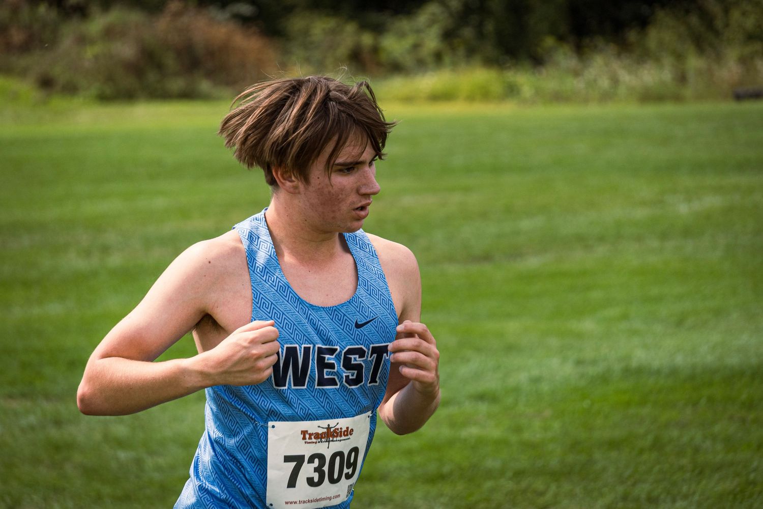 Cross country runners compete on a grassy course during a sunny autumn race meet.