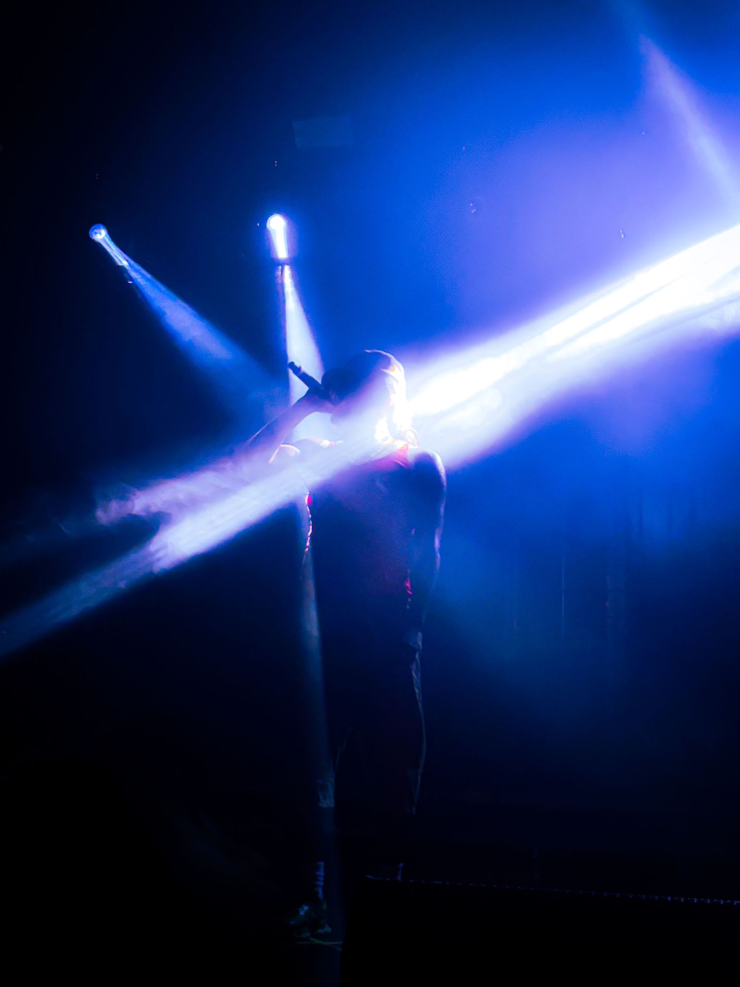 Blue laser beams pierce through fog creating dramatic light rays in a dark performance space.