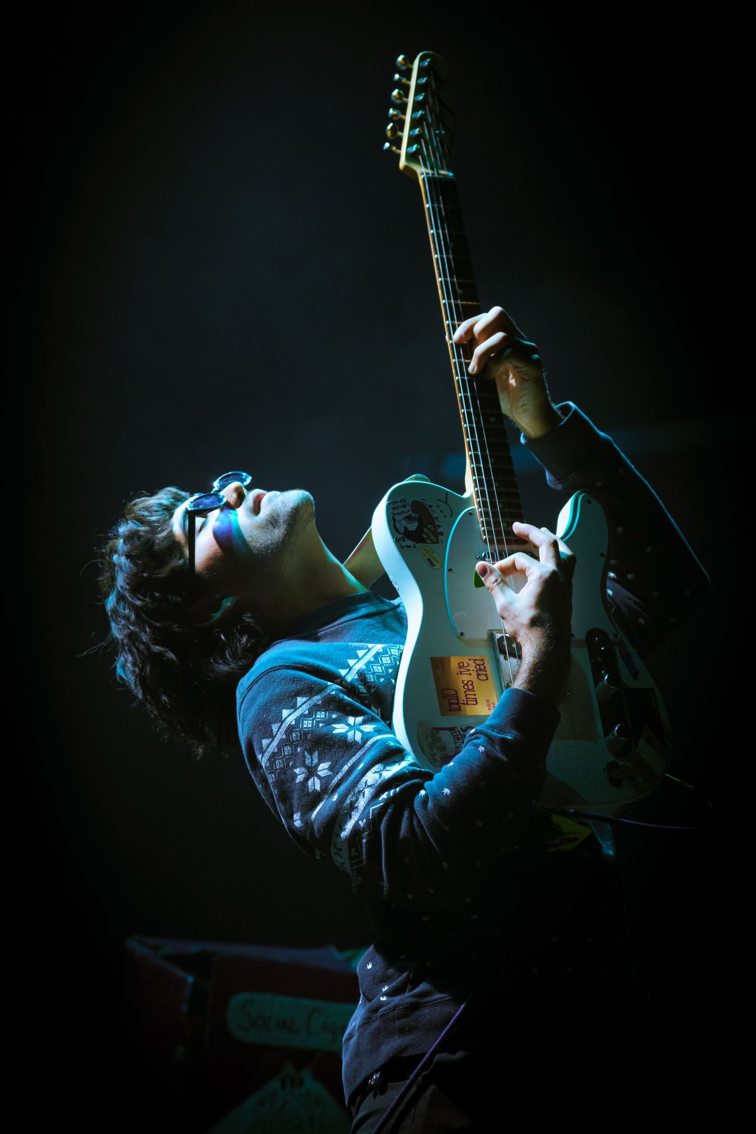 A series of moody blue-lit photographs showing a guitarist lying back while playing an electric guitar in a dark setting.