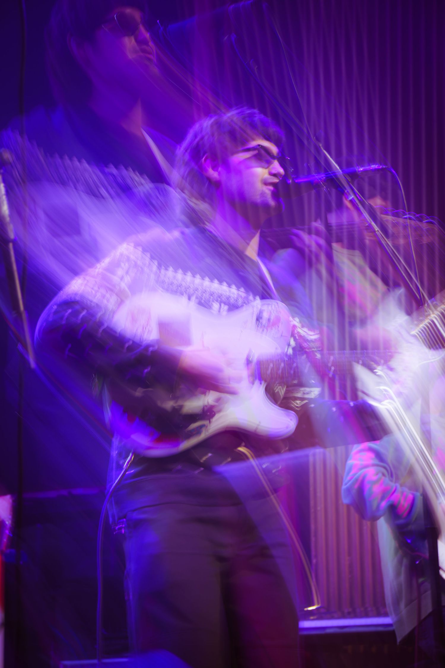 Long exposure photograph captures dynamic movement in purple lighting during a live performance on stage.