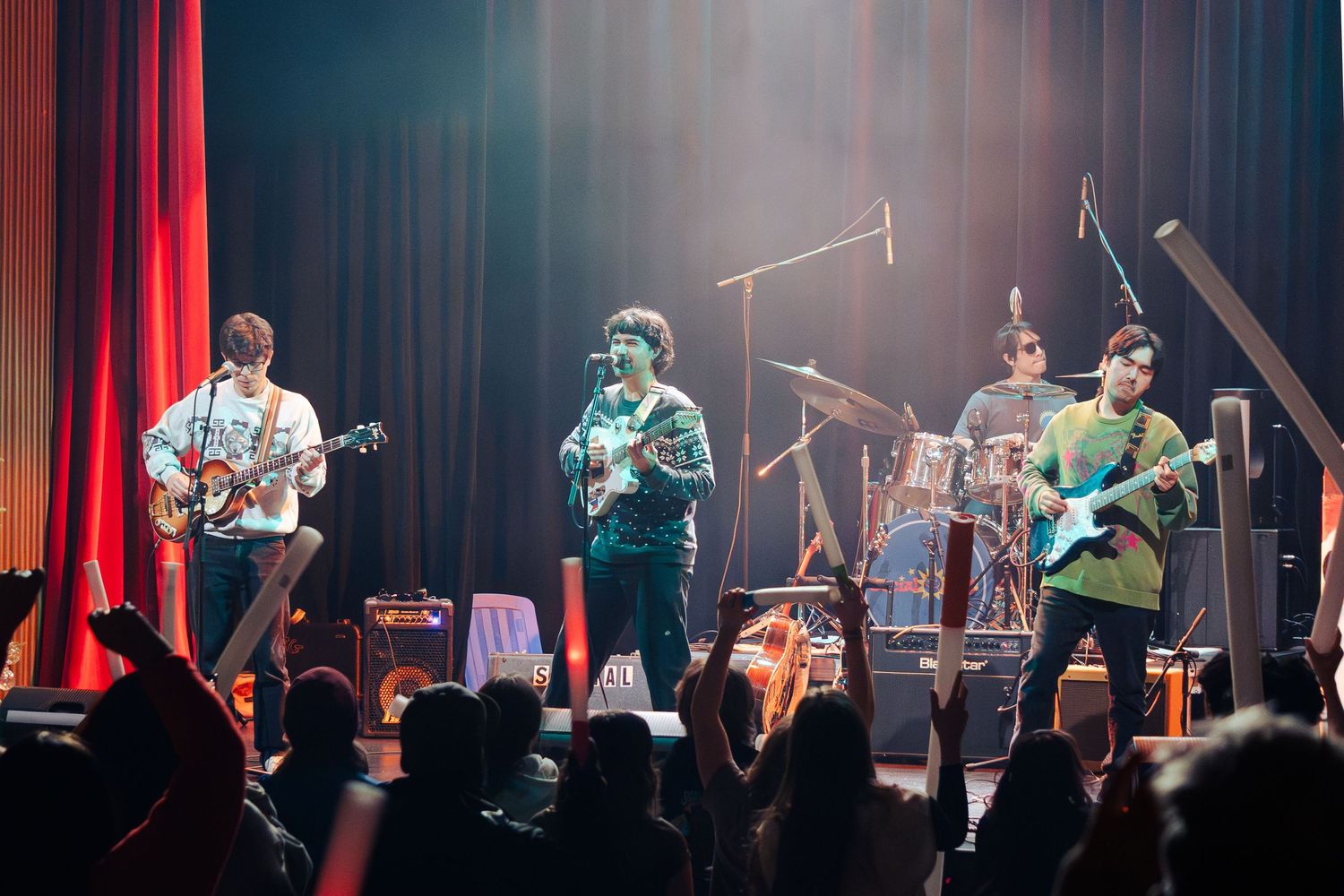Orchestra musicians performing on stage with dramatic red lighting and curtains during a live concert performance.
