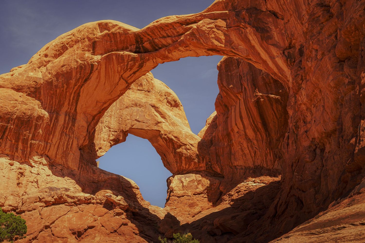Hiker stands beneath the iconic Double Arch sandstone formation at Arches National Park, Utah, under a clear blue sky.