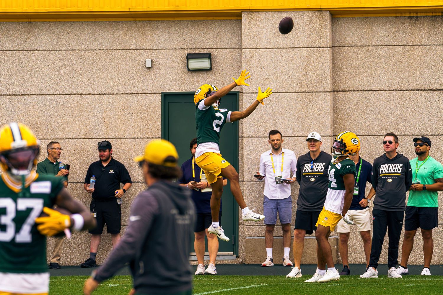 Green Bay Packers player leaps to catch a football during an outdoor NFL training camp practice session.