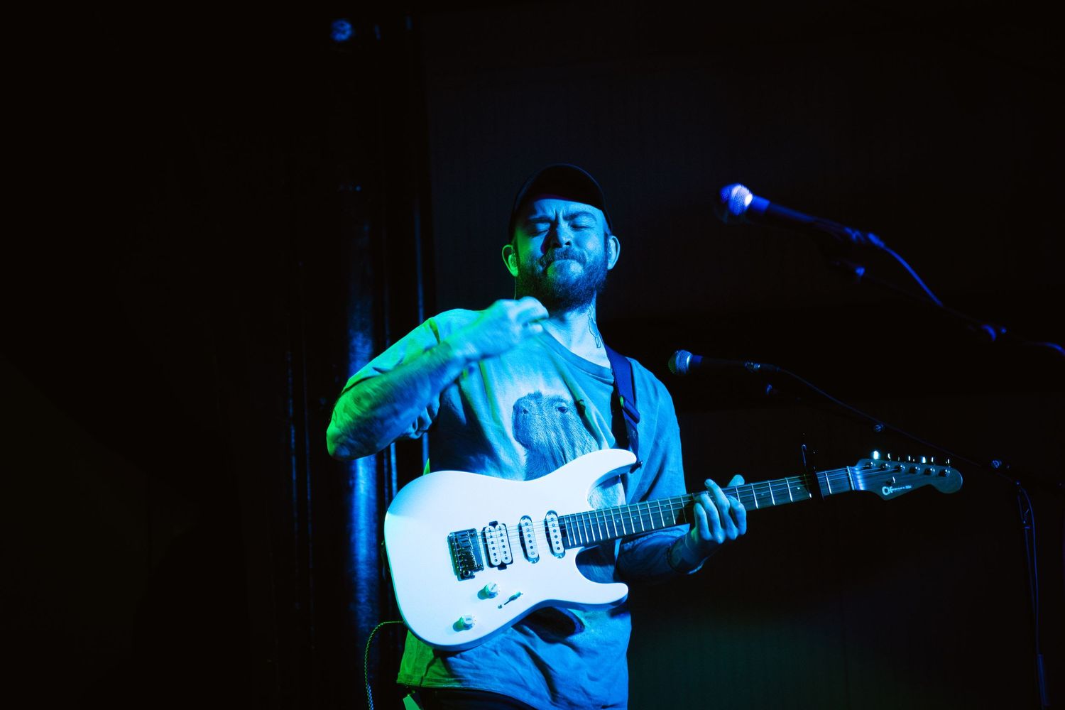Musicians perform on stage with electric guitars in a dark venue illuminated by blue lighting effects.