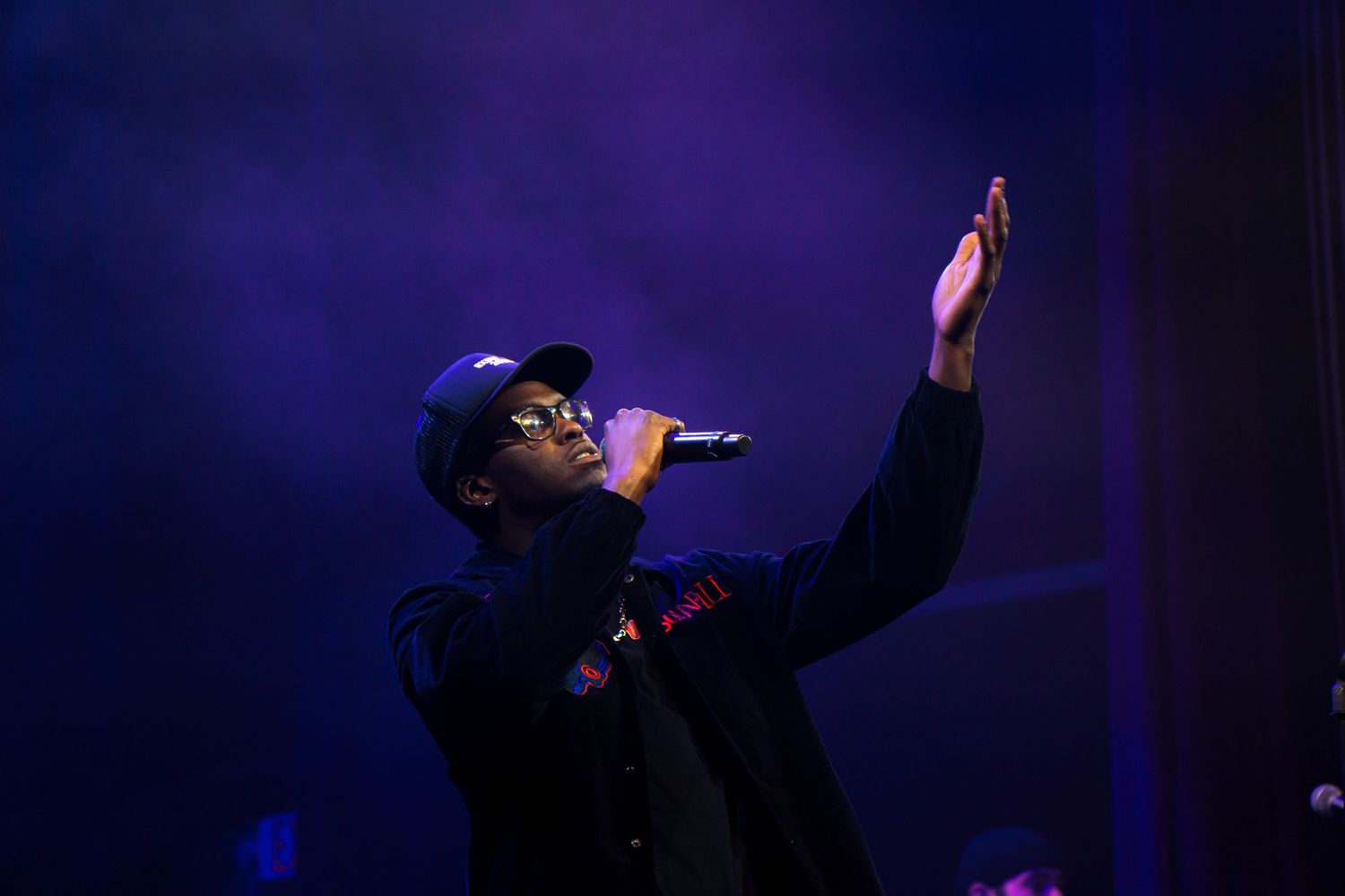 A performer sings passionately on stage with dramatic purple lighting creating a silhouetted effect during a concert performance.