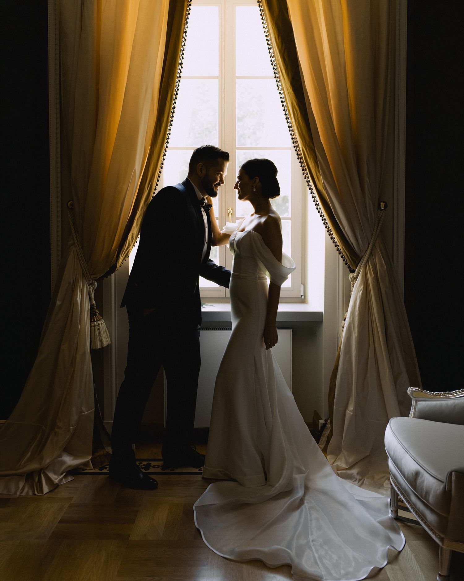 A series of silhouettes against a window with yellow curtains shows a couple in wedding attire creating dramatic shadows.