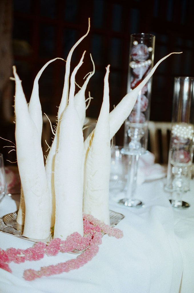 White taper candles with dried branches arranged on a table with pink floral accents and crystal glassware.