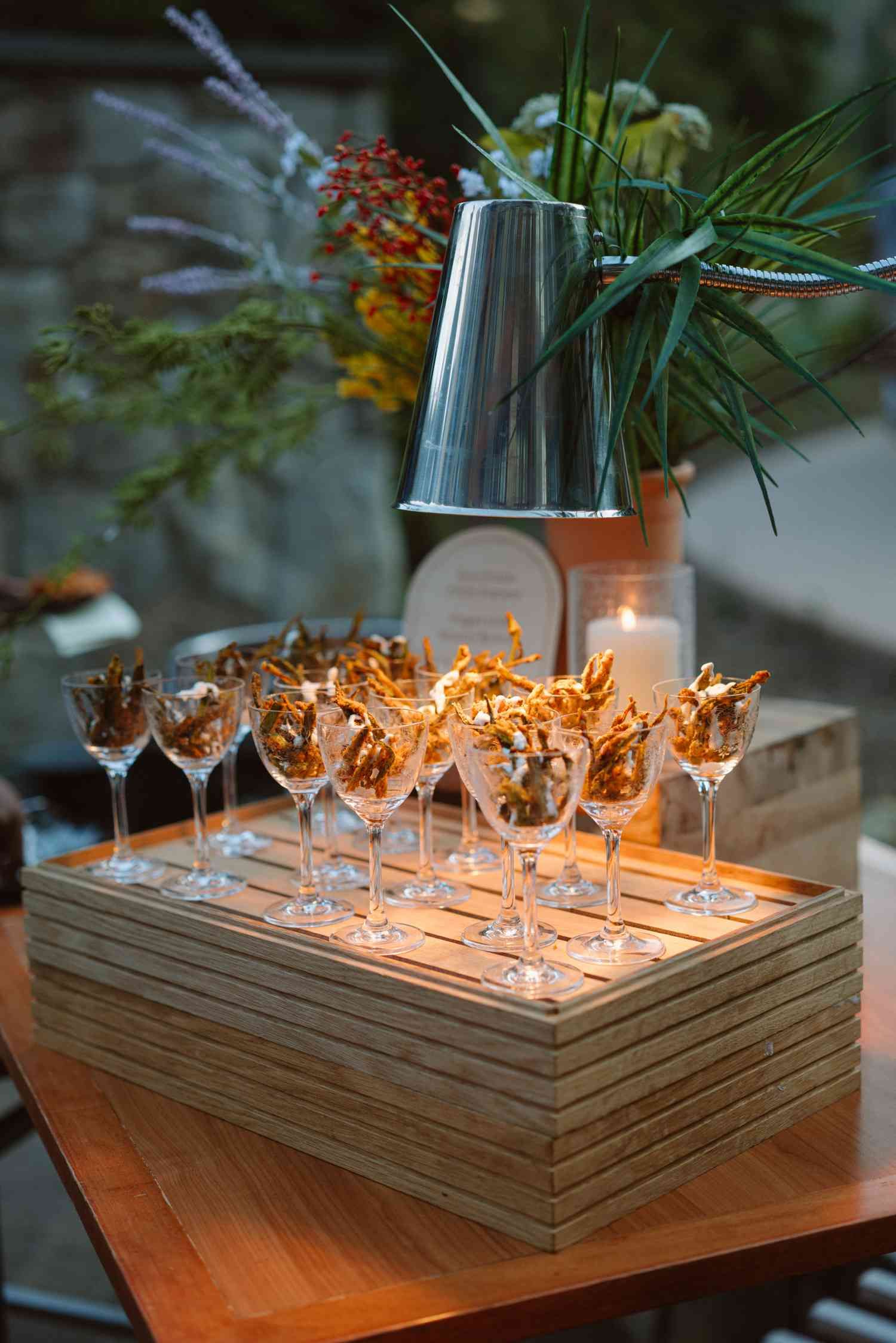 A modern wooden centerpiece display with wine glasses and candles arranged in a geometric pattern glows warmly on a table.