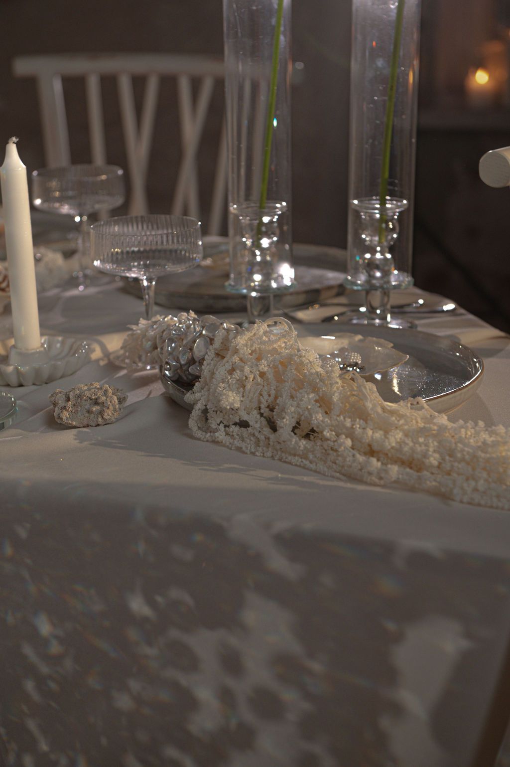 Elegant white wedding table setting with candles, crystal glassware, and decorative lace details on a white tablecloth.