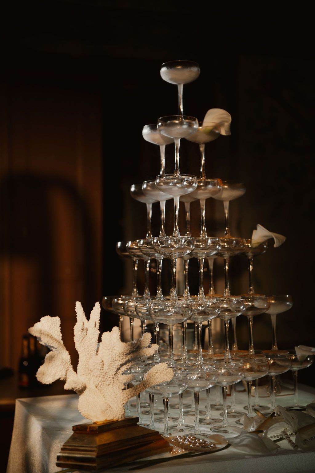 Elegant champagne tower with stacked crystal glasses and white coral decorations at a formal event.
