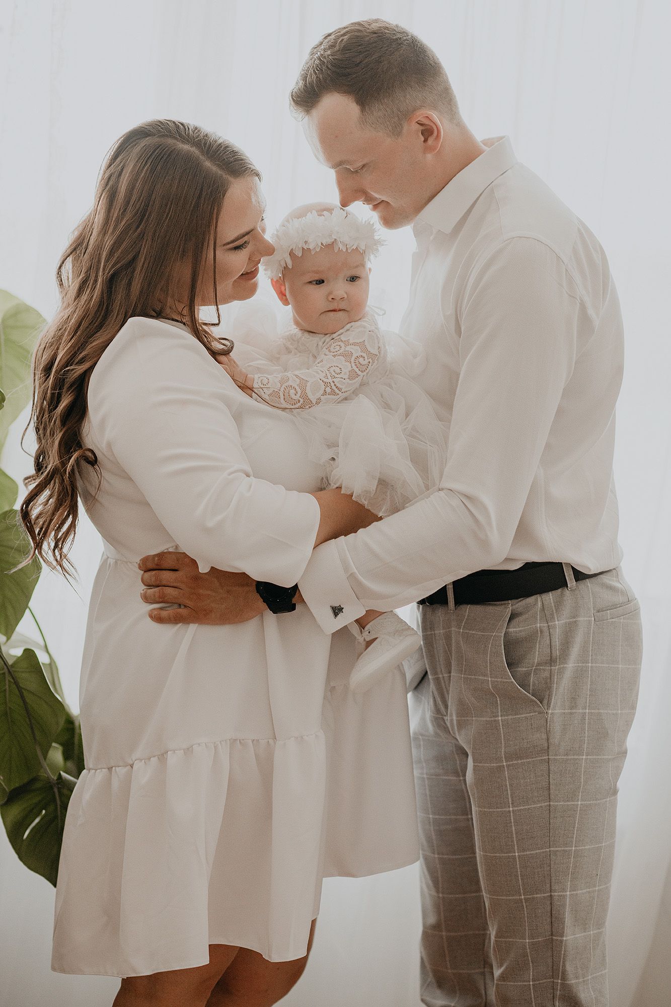 Family wearing coordinated white outfits embraces tenderly during an intimate indoor photo session.
