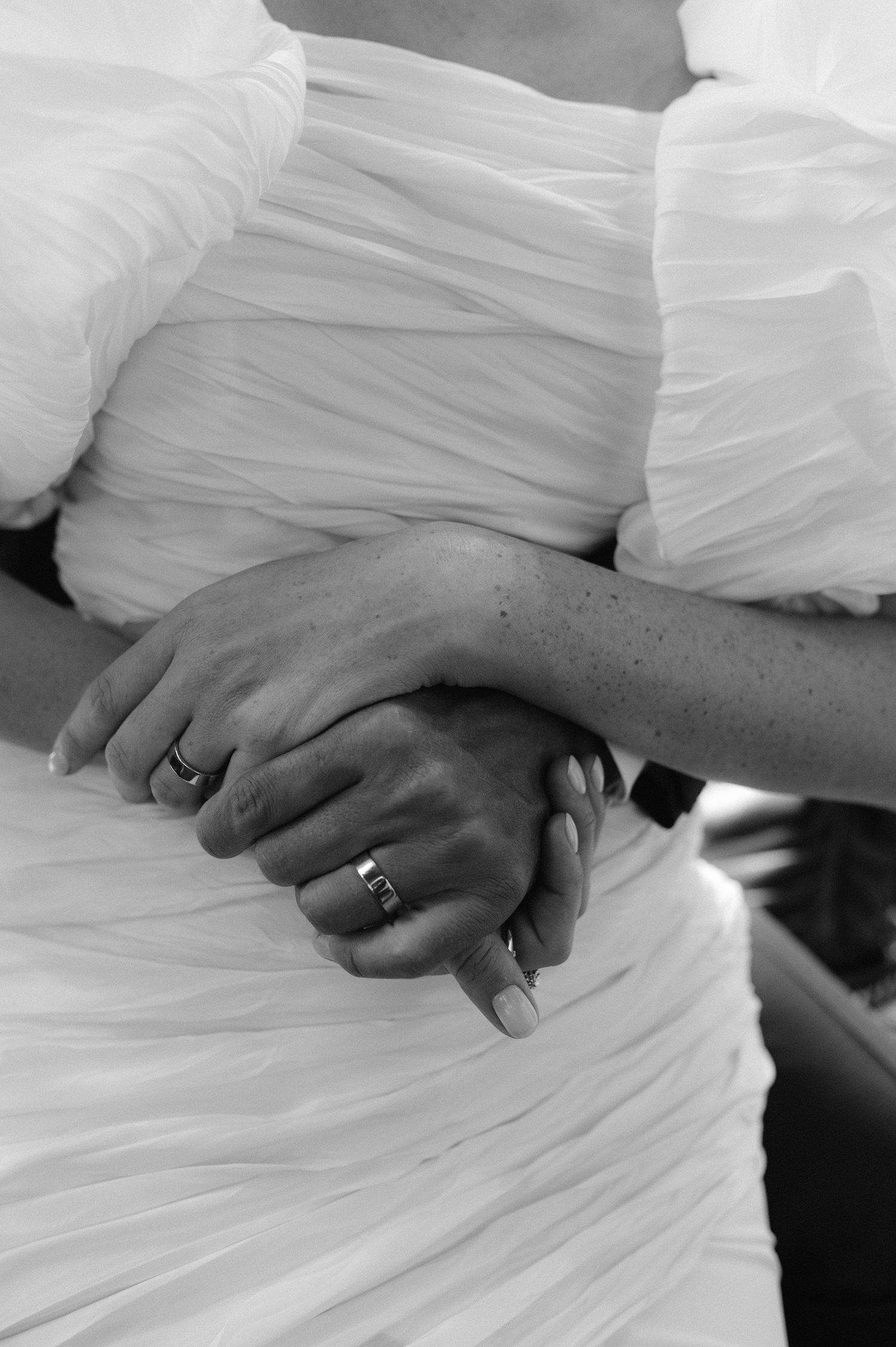 Close-up detail of hands with wedding rings against white tulle fabric.