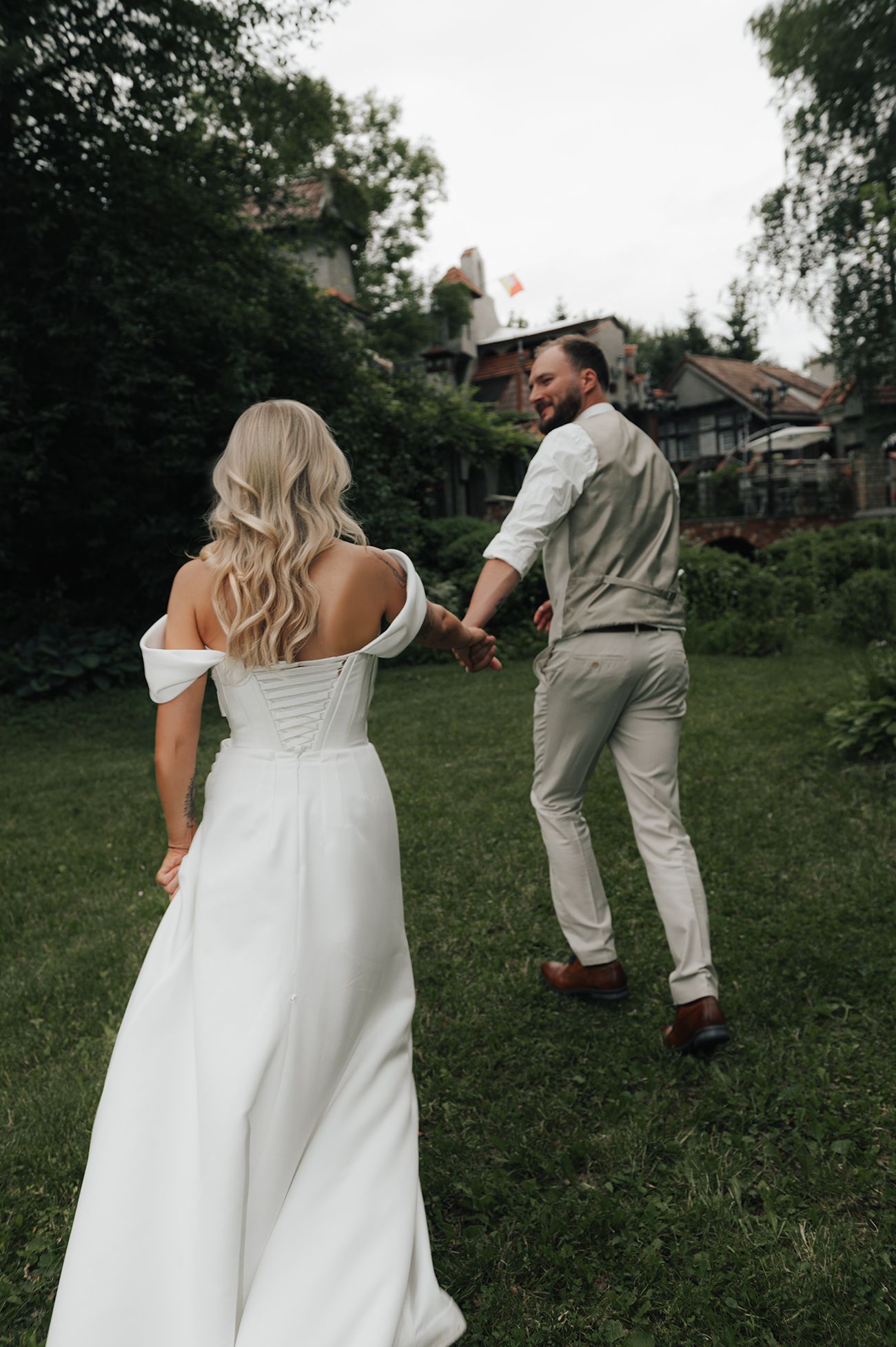 Couple in wedding attire playfully poses in a grassy outdoor setting with trees in the background.