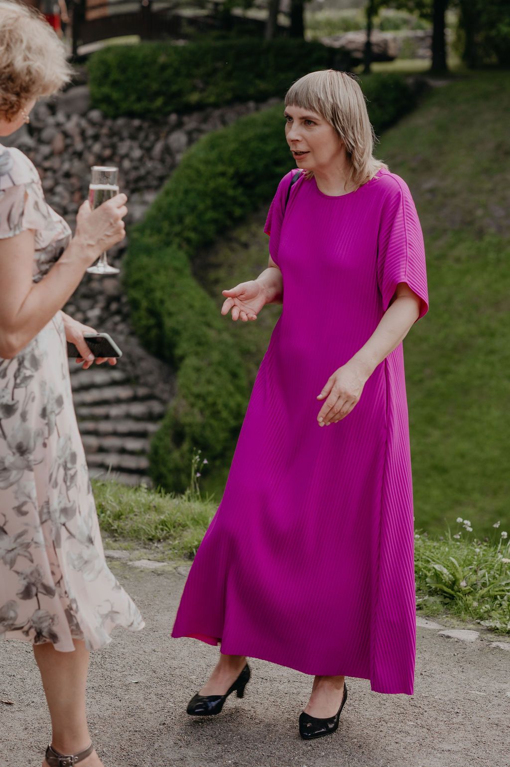Wedding guest in vibrant magenta dress conversing outdoors at garden reception.
