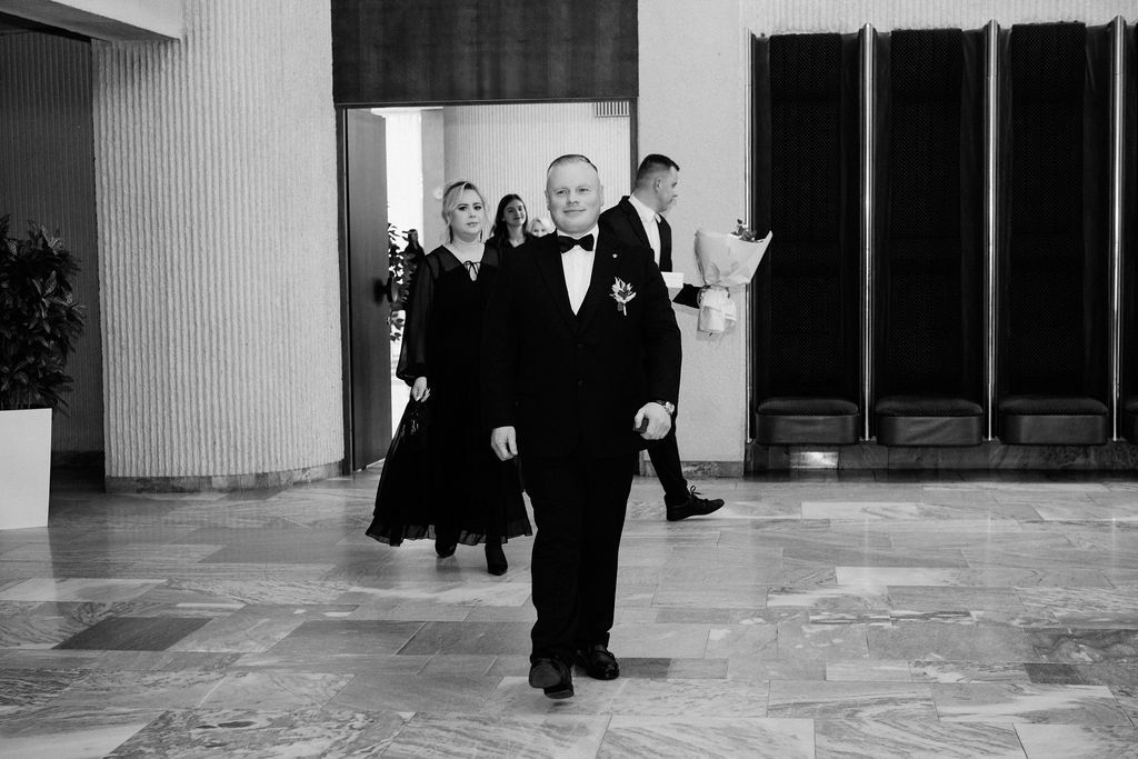 Elegant guests in formal attire walk through a grand hall at a black-tie wedding reception.