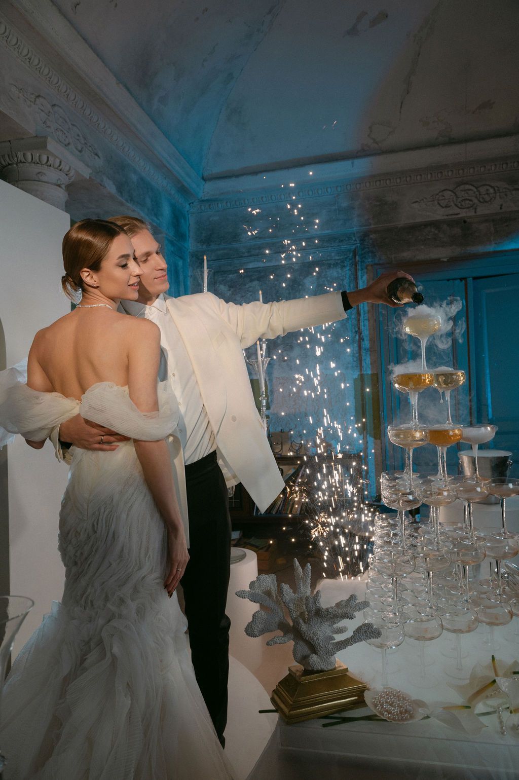 Bride and groom pouring champagne tower with sparkling fireworks at elegant wedding reception.