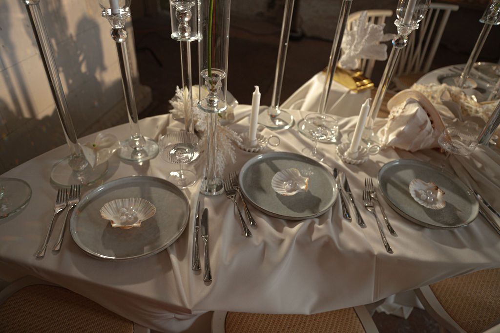 Elegant white wedding table setting with silver plates, crystal glasses, candles, and white napkins for a formal dinner.