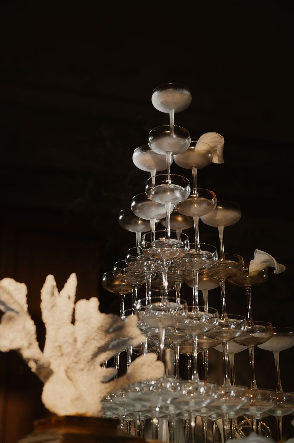 Elegant champagne tower with coupe glasses and white floral decor against dark background at luxury event.