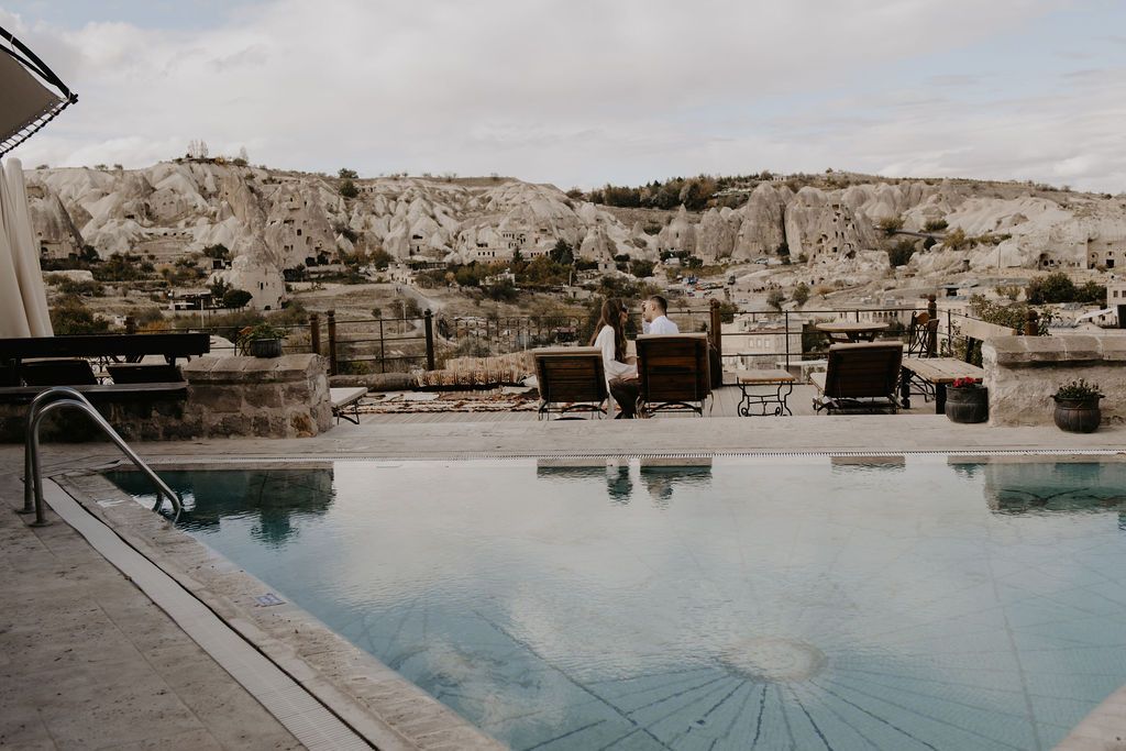 Luxury infinity pool overlooking rocky Cappadocia landscape with lounge chairs and cave formations in background.