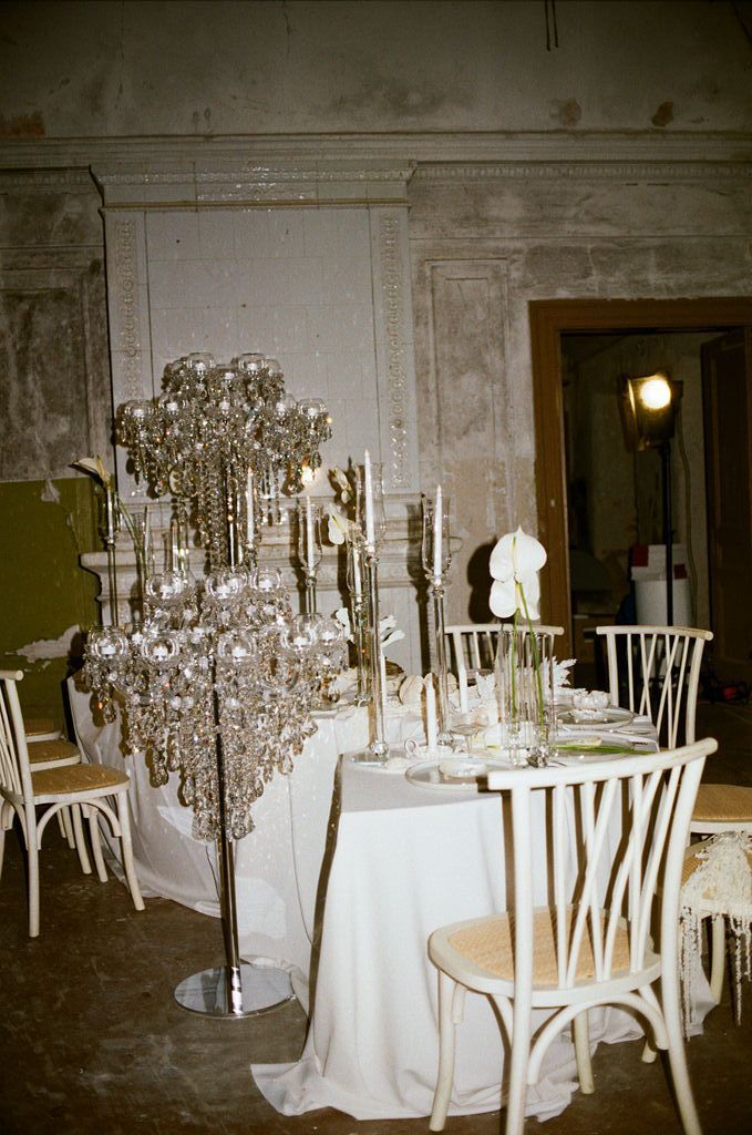 Elegant wedding reception table with crystal candelabra centerpiece, white linens, and wooden chairs in ornate venue.