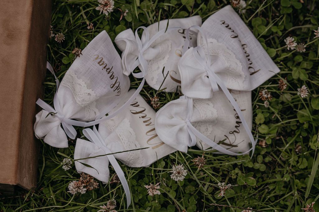 White ribbon bow favors with handwritten script text arranged on green grass with clover flowers.