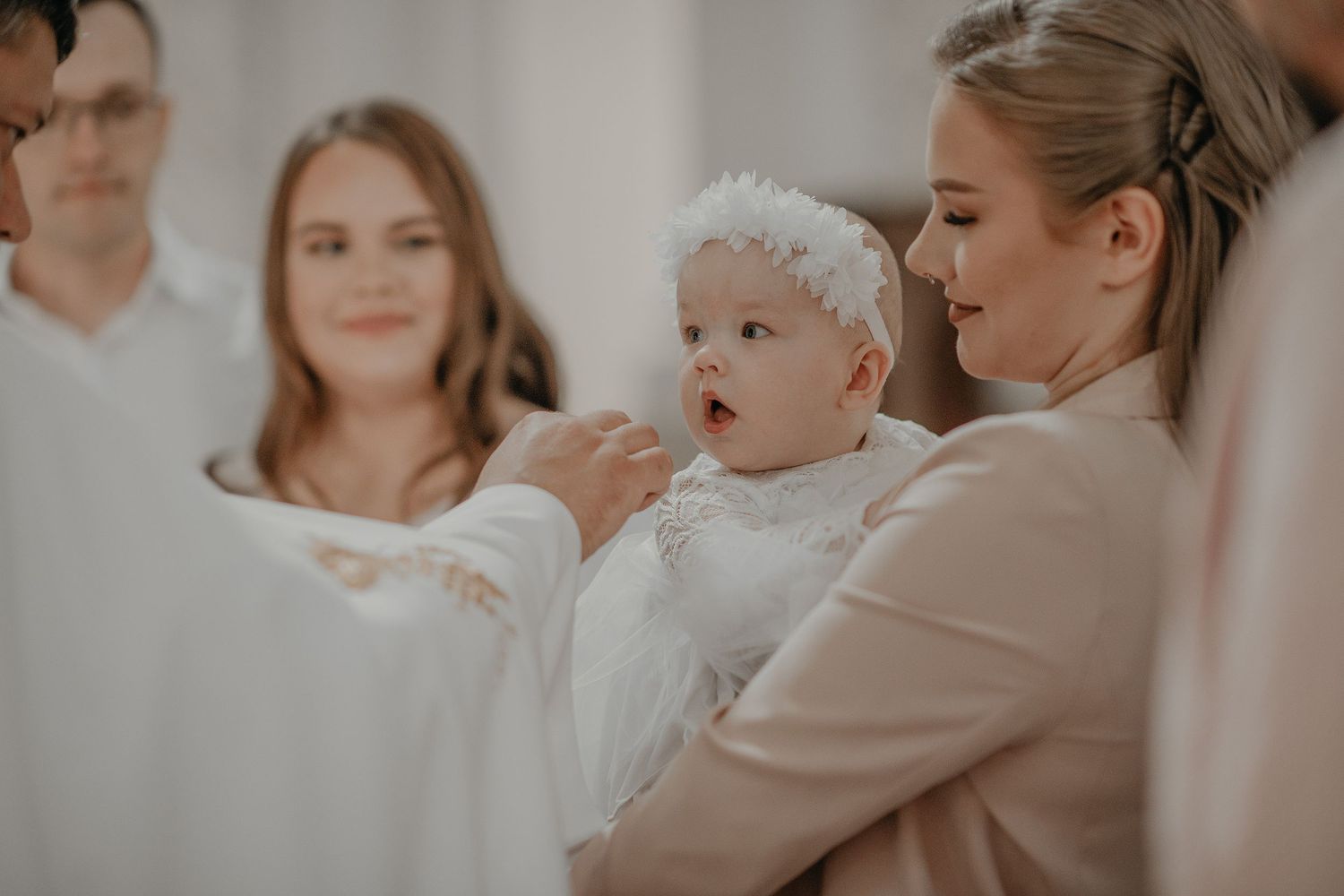 A group of people dressed in light colors gather together in a soft, warm-toned indoor setting.