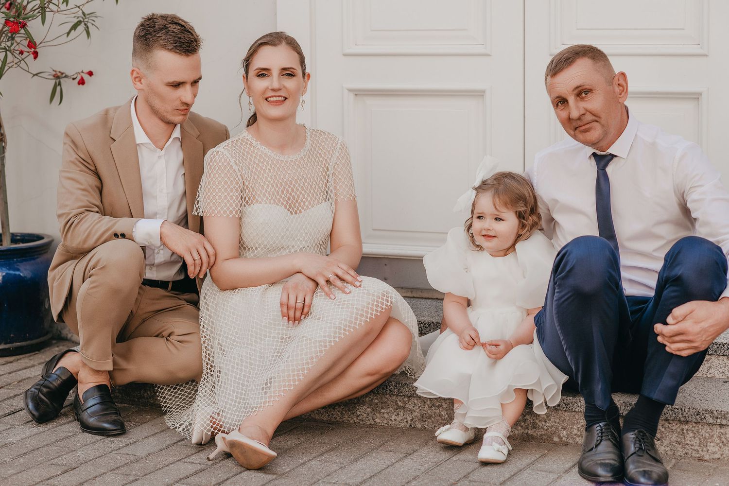 A group sits together on stone steps wearing formal attire in beige and white tones during a special occasion.