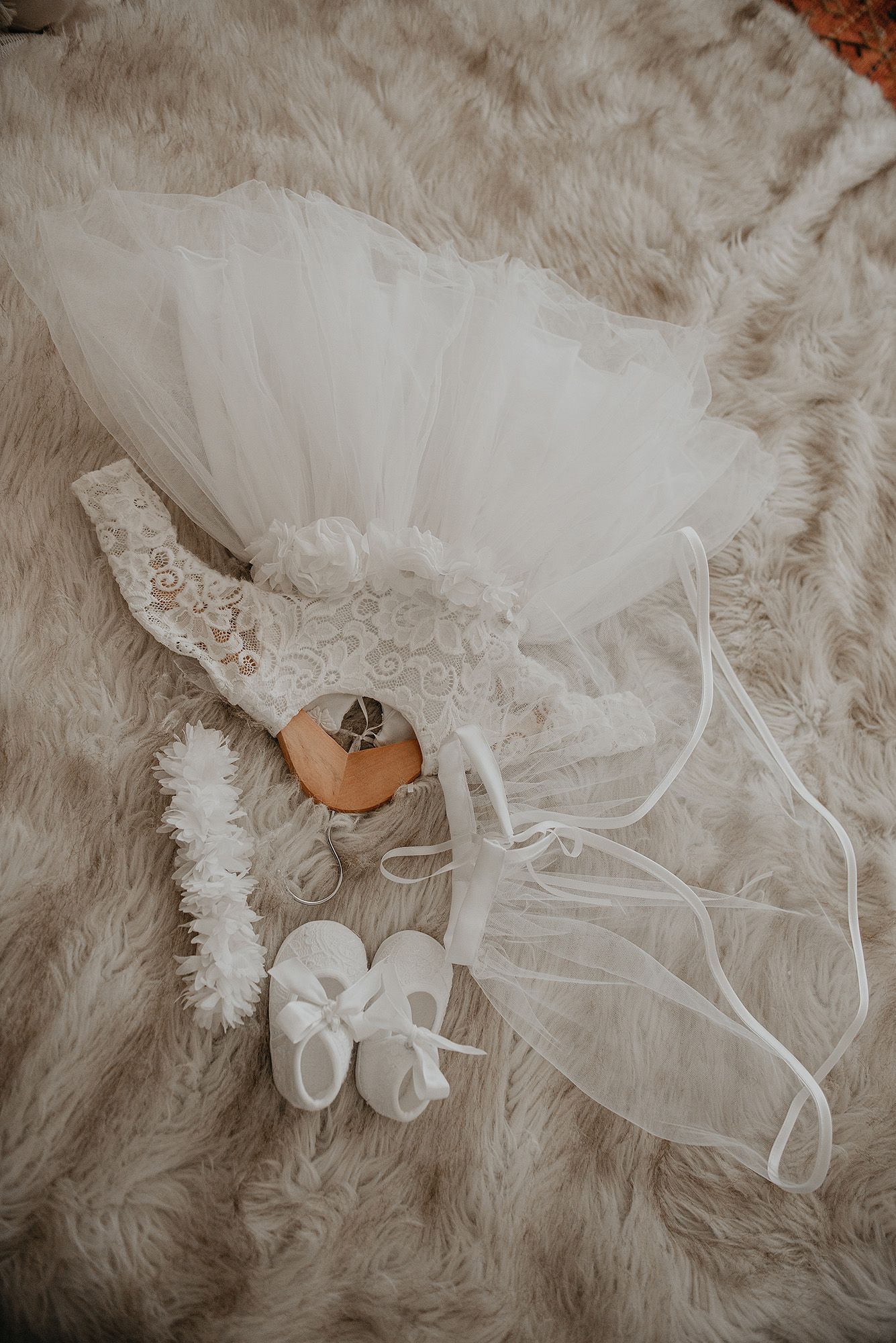 White tulle tutu skirt, baby shoes, and wedding rings displayed on soft fur background in ethereal bridal styling.