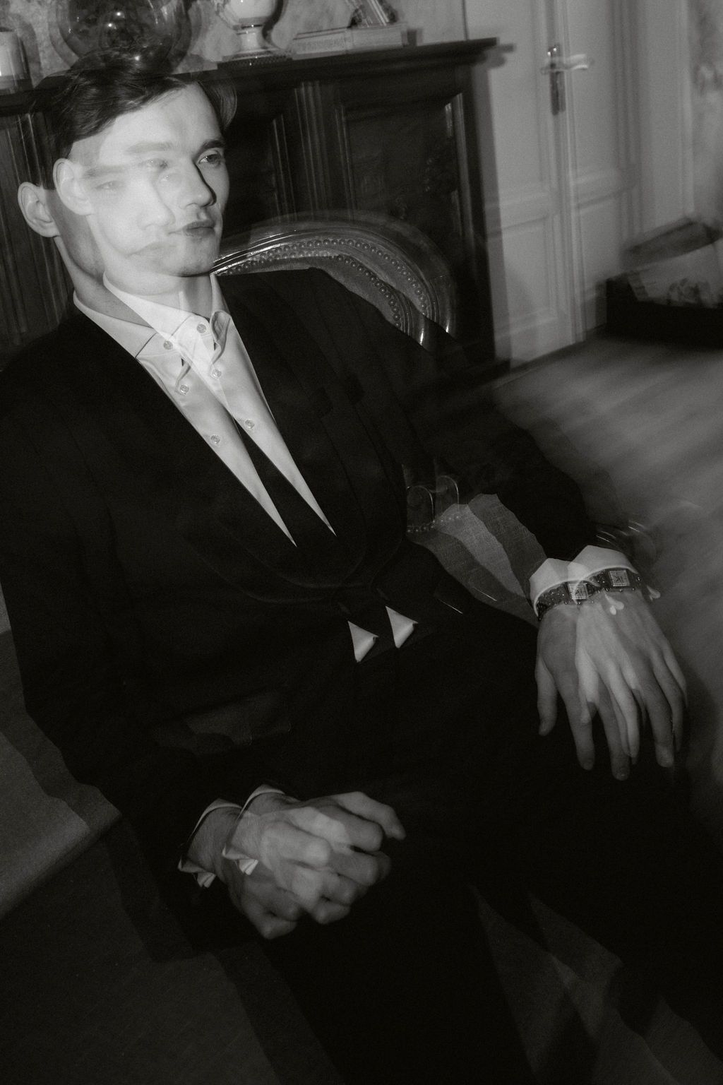 Black and white double exposure photo of a man in a dark suit sitting in a chair in an elegant room.