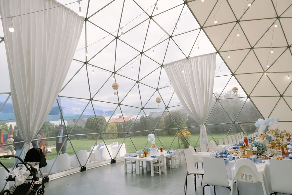 Elegant geodesic dome event venue with white draping, dining tables, and panoramic views of green landscape.